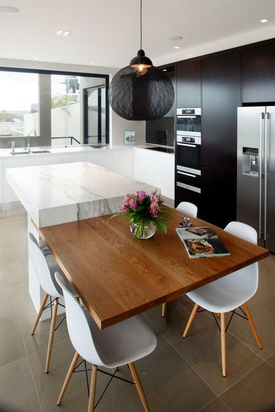 a black kitchen with a white marble kitchen island and an additional tabletop for having meals
