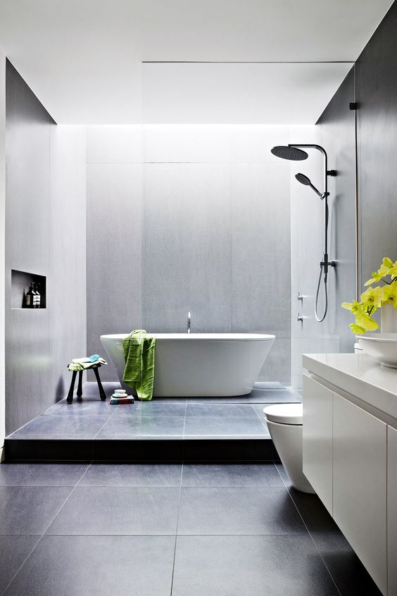 a clean modern space with grey and black tiles, a free-standing tub, a white vanity and a skylight