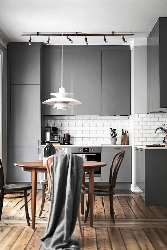 a modern grey kitchen with a subway tile backsplash and a wooden dining set for a contrast