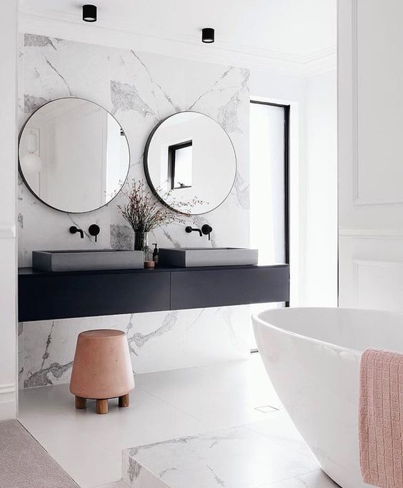a modern space with white marble, a black vanity, a free-standing bathtub and concrete sinks looks chic