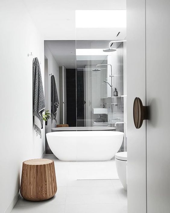 A modern white space with a free standing tub, white fixtures and a wooden stool