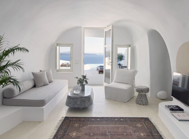 The living room in pure white features a platform sofa, a chair and an eye catchy stone table, a couple of windows with cool views