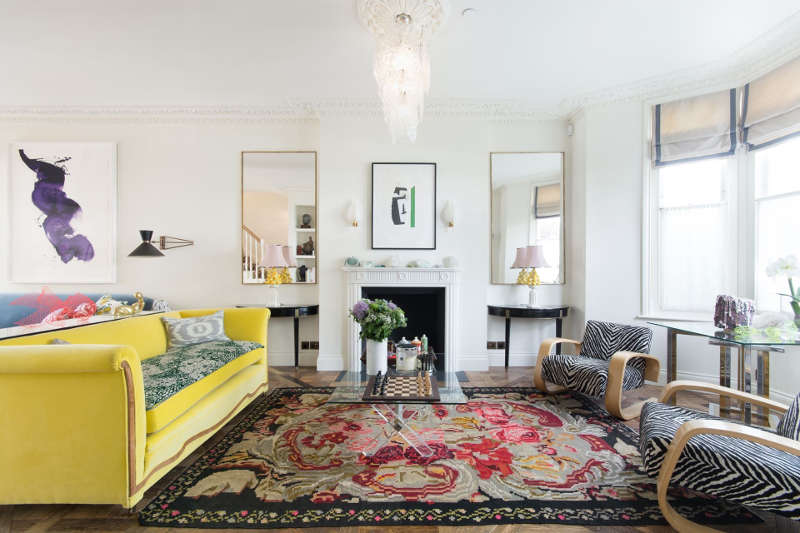 This gorgeous living room is done with a bold yellow sofa, animal print chairs, a gorgeous vintage chandelier and an antique fireplace