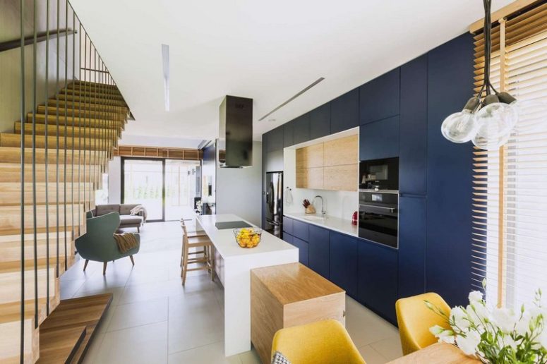 The kitchen is done with sleek navy cabinets, light-colored wood and a long kitchen island that features a breakfast zone
