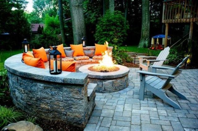 a gorgeous firepit zone with a round stone bench, candle lanterns and orange pillows for a fall feel