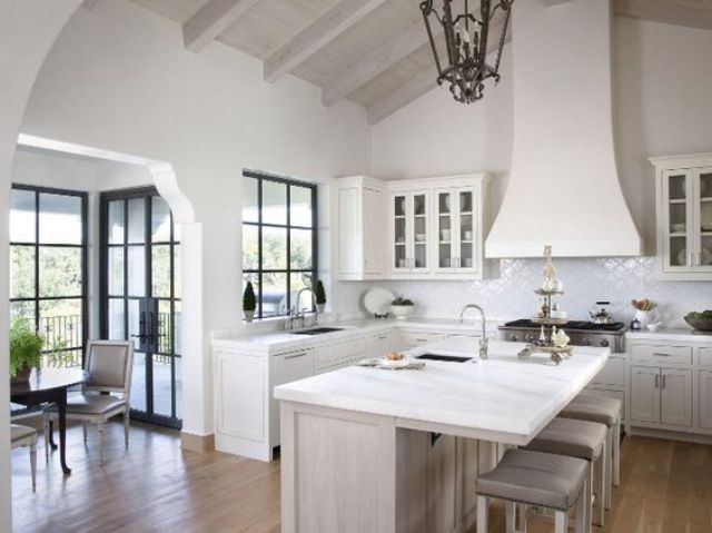 a white vintage farmhouse kitchen with a large hood, vintage lamps and a chic kitchen island