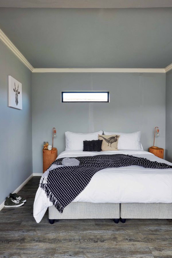 The bedroom is small and simple, with a reclaimed wood floor, blue walls and ceiling and wooden stump nightstands with bulbs
