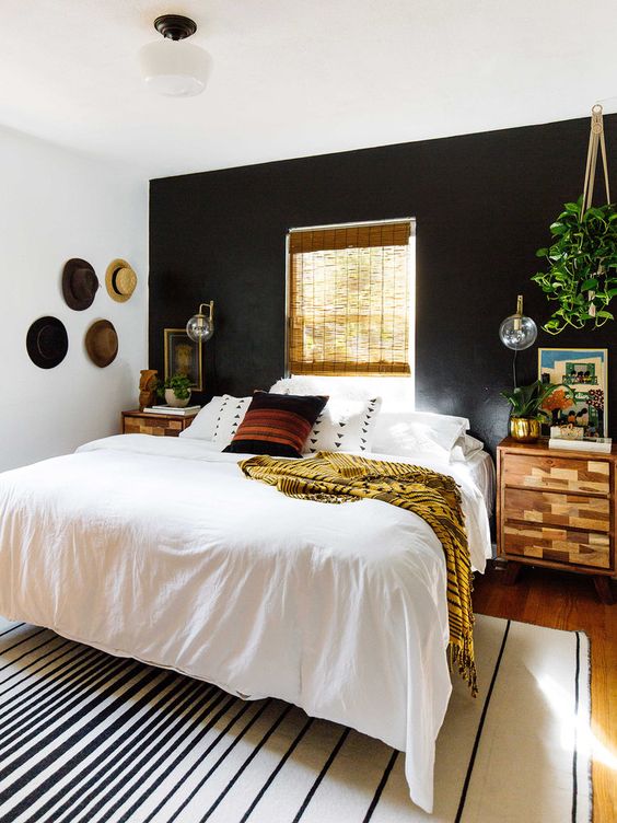 a boho and rustic space with a black headboard wall is balanced with warm-colored wood and a window in this wall