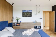 05 The master bedroom features a wooden slat wall and a floating sideboard and a blue upholstered bed