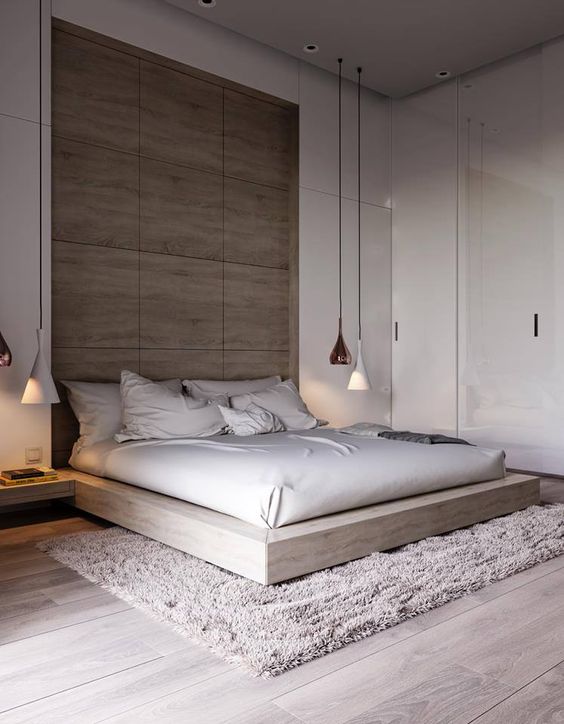 a modern space with glossy white walls, a wooden headboard wall, a wooden platform bed and white and copper hanging lamps