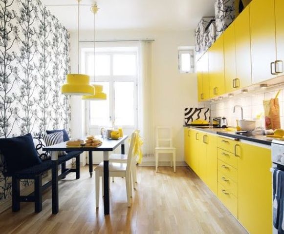 a small modern yellow kitchen with dark countertops, a dining zone accentuated with printed wallpaper