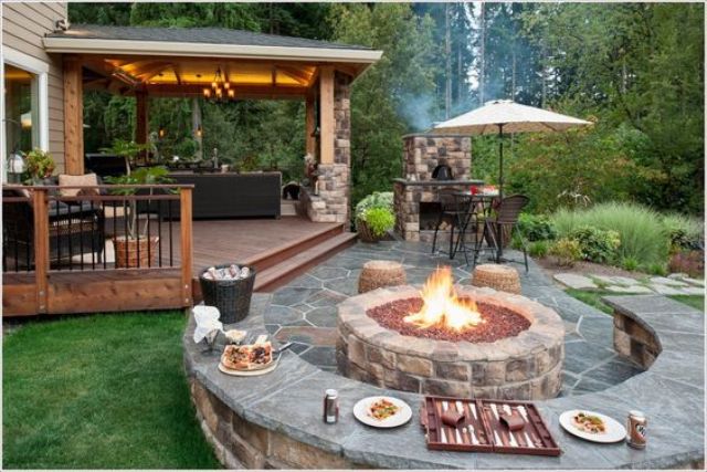a stone part of the patio is decorated with a rounded bench and tabletop in one and a gorgeous firepit for cooking