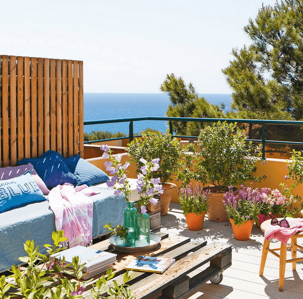 The terrace is decorated with some stools, a pallet table, a daybed and lots of potted flowers and greenery