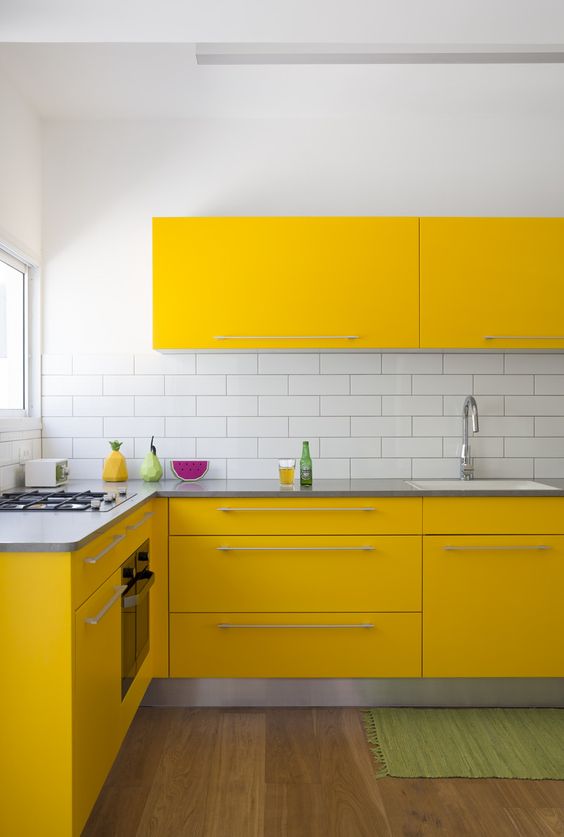 a modern yellow kitchen with stainless steel countertops and a white tile backsplash looks very eye-catchy