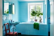 07 The bathroom is clad with bold blue tiles, there’s potted greenery and some green towels, a mid-century modern chair is red