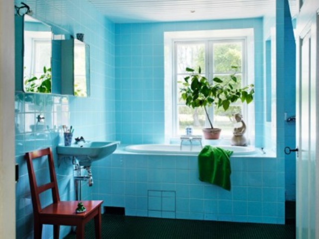 The bathroom is clad with bold blue tiles, there's potted greenery and some green towels, a mid-century modern chair is red