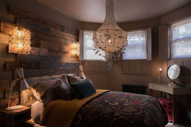 The master bedorom is done with a reclaimed wood headboard, an oversized chandelier and colorful textiles