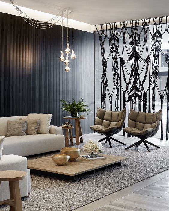 a cool modern space with a black wooden wall, neutral furniture and a black macrame space divider to make it bolder