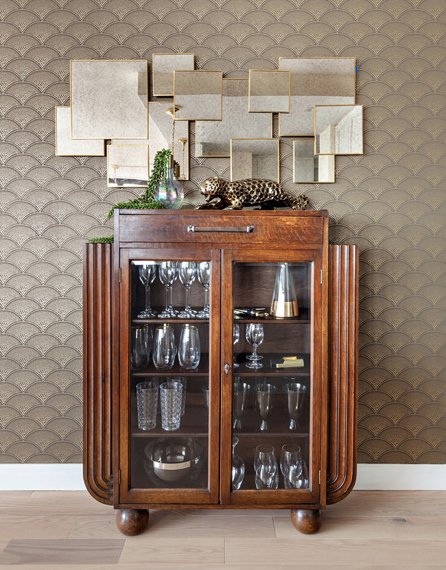 A cool wooden and glass bar cabinet with a geo mirror over it added to the interior