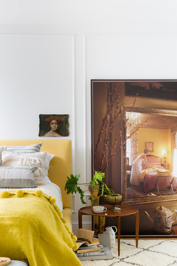 The master bedroom raises the mood with cool artworks and a sunny yellow upholstered bed