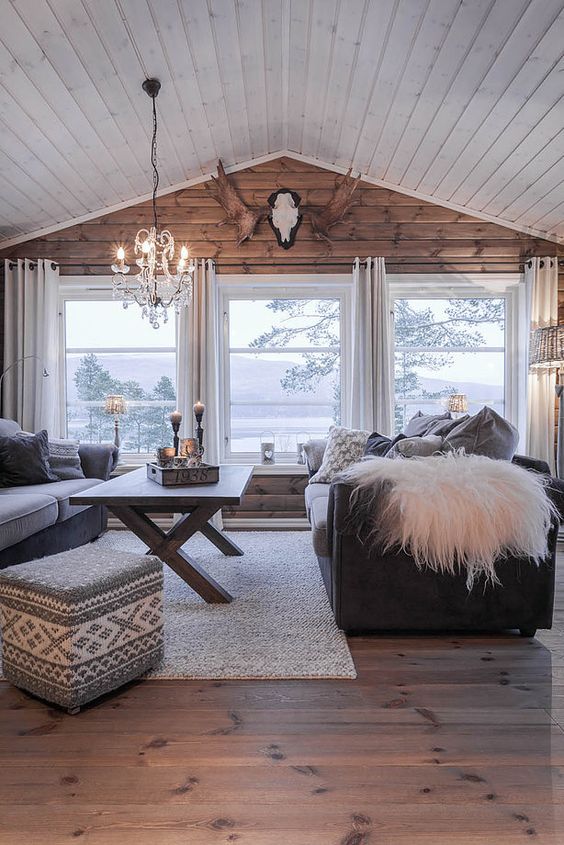 a cozy cabin-style living room with a wooden wall and several windows that bring views in