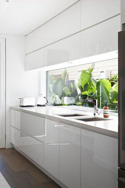 a minimalist white kitchen with a unique window backsplash which brings much light and views in
