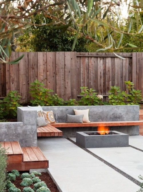 a concrete and wood L-shaped bench and a fire pit in a mmodern backyard