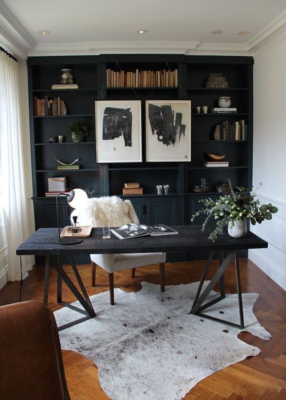 A cozy home office with a black shelving unit that takes a whole wall, an amber colored wooden floor