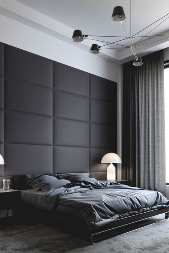 a moody space with a black upholstered wall, a dark bed and dark linens, curtains and a rug that match