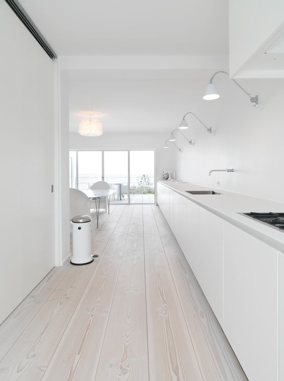 a large long minimalist white kitchen with only floor cabinets and whitewashed floors
