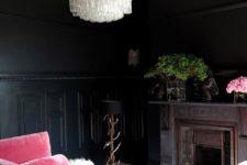a luxurious moody living room with black walls, a crystal chandeliers, a pink sofa and a vintage fireplace