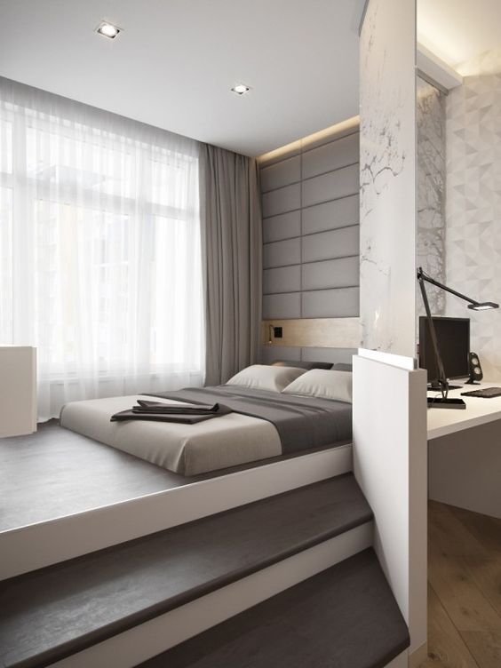 a grey upholstered wall, matching linens and a glass partition that separates the sleeping space form the working one