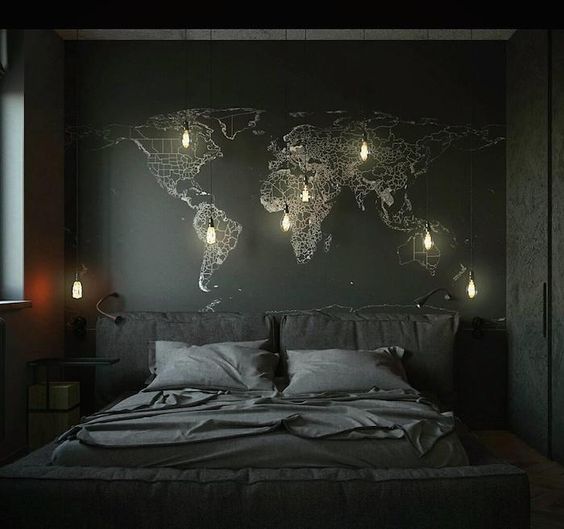 a moody space with a black wall and a world map on it, a black upholstered bed and some hanging bulbs