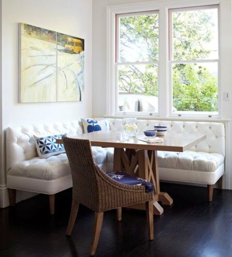 a white diamond upholstery corner bench contrasts a wicker chair and a wooden table