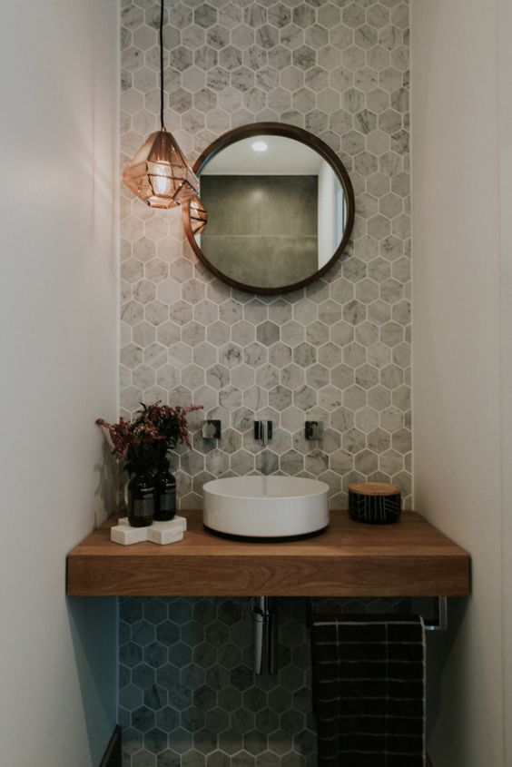 An accent wall with marble hexagon tiles and a wooden vanity make the space eye catchy