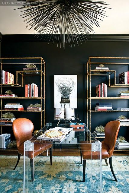a chic shared home office with a statement black wall, an acrylic desk and brass touches