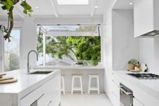 18 a light white kitchen with marble surfaces and a large window that is extended outdoors as a meal space