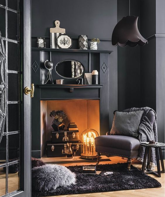 A modern space with a vintage feel, black walls and furniture, a faux fireplace with a unique lamp and some vintage accessories