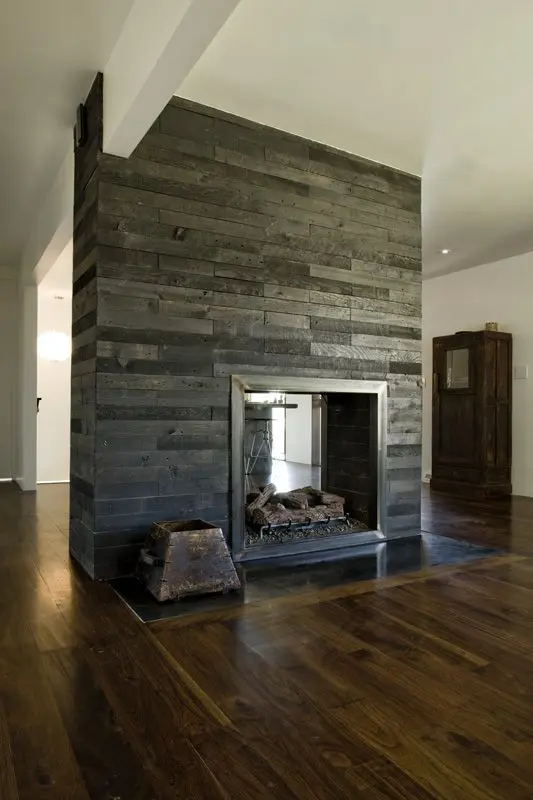 A double sided fireplace clad with reclaimed grey and black wood brings texture and a cool look to the space