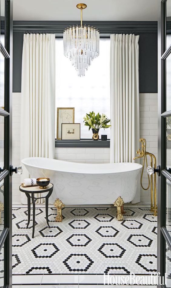 a refined crystal chandelier, a bathtub on clawfeet, brass fixtures and creamy curtains add a glam feel to the space