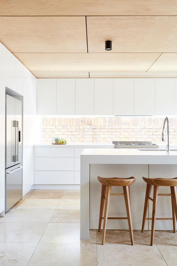 a minimalist white kitchen with a wooden ceiling, stools and an eye-catchy backsplash