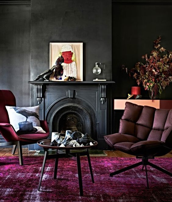 A moody space with black walls, a fuchsia rug and furniture and artworks
