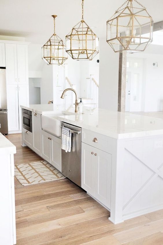 a modern farmhouse kitchen with brass lamps and details and stainless steel appliances