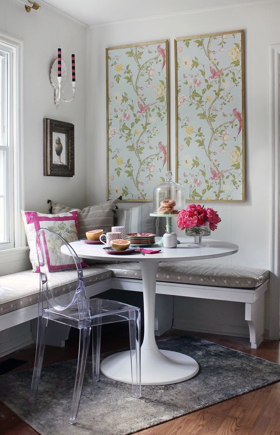 a wall-mounted corner bench with a cushion on top, an acrylic chair and floral artworks for a cheery breakfast nook