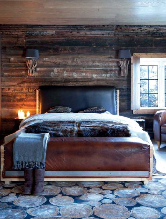 A cabin inspired bedroom with a dark stained wooden wall, a leather bed and a rug that imitates wood slices