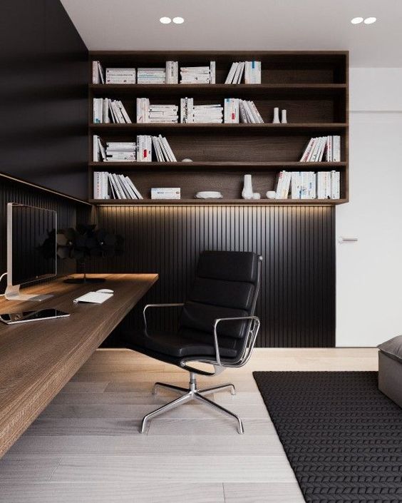 A modern masculine space with black wood panel walls and a lit up wall shelving unit, a wall mounted desk