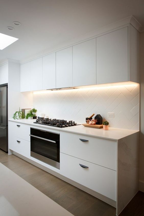 a modern white kitchen is made more eye-catchy with lights and a geometrically clad backsplash