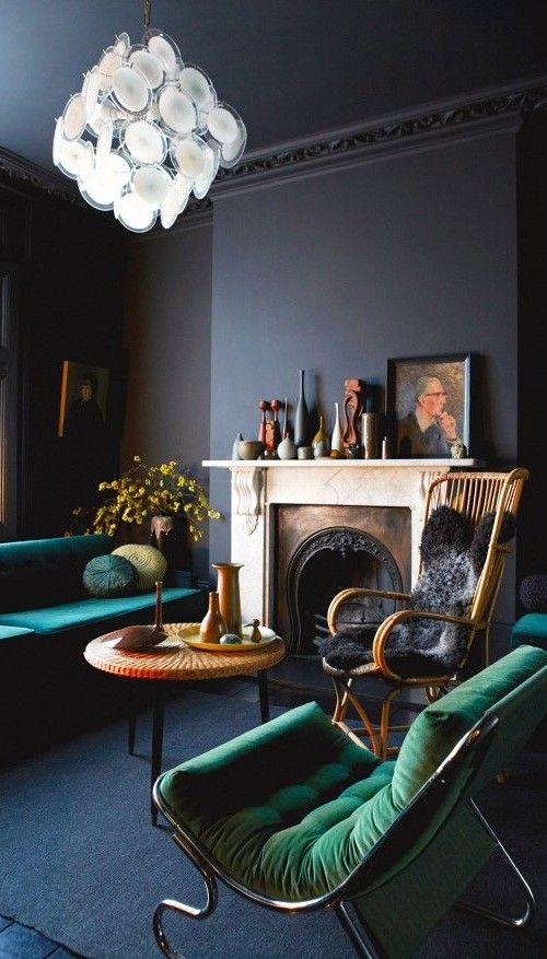 a refined dark living room with black walls, amarald upholstered furniture, a vintage fireplace and some beautiful vases