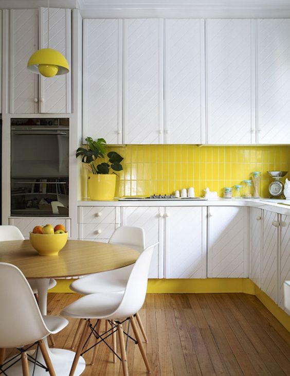  a white kitchen is enlivened with a neon yellow tile backsplash, lamps and a planter
