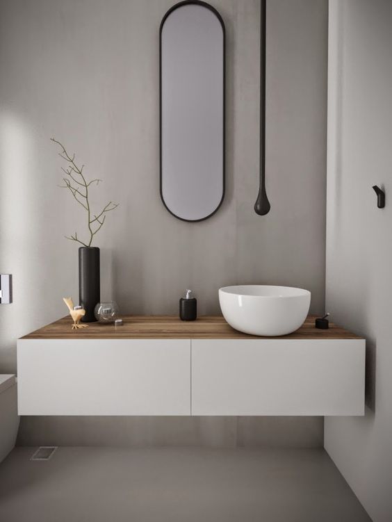 A minimalist white vanity with a light colored wooden top and a bowl sink